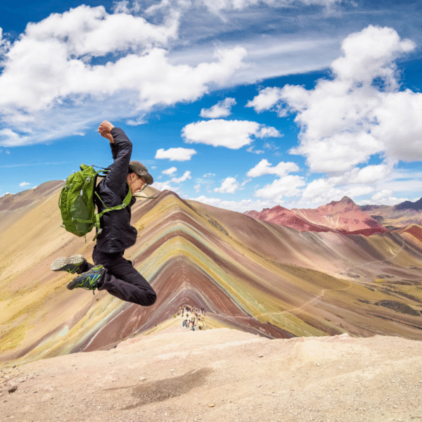 una persona saltando en la cima de la Montaña de los Siete Colores, también conocida como Vinicunca o Montaña Arcoíris, ubicada en los Andes peruanos, cerca de Cusco