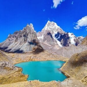 Laguna de color turquesa vibrante en medio de montañas nevadas en el circuito de trekking del Nevado Ausangate, Perú