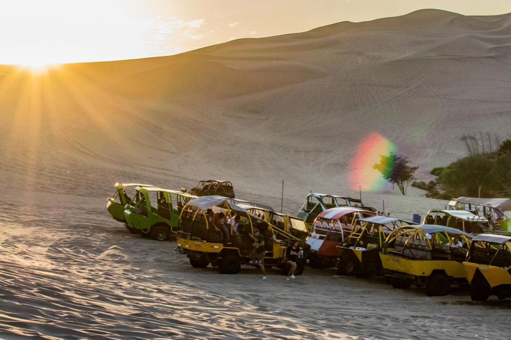 Carros areneros recorriendo las dunas del desierto de Huacachina en Ica, Perú, con atardecer espectacular