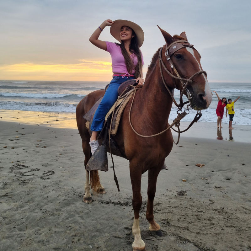 Turista con sombrero de paja disfrutando de un paseo a caballo por la orilla de la playa durante el atardecer