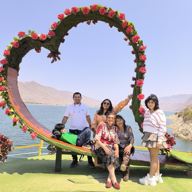 Familia de turistas posando dentro de una gran estructura de corazón decorada con rosas frente al embalse de la Represa de Gallito Ciego