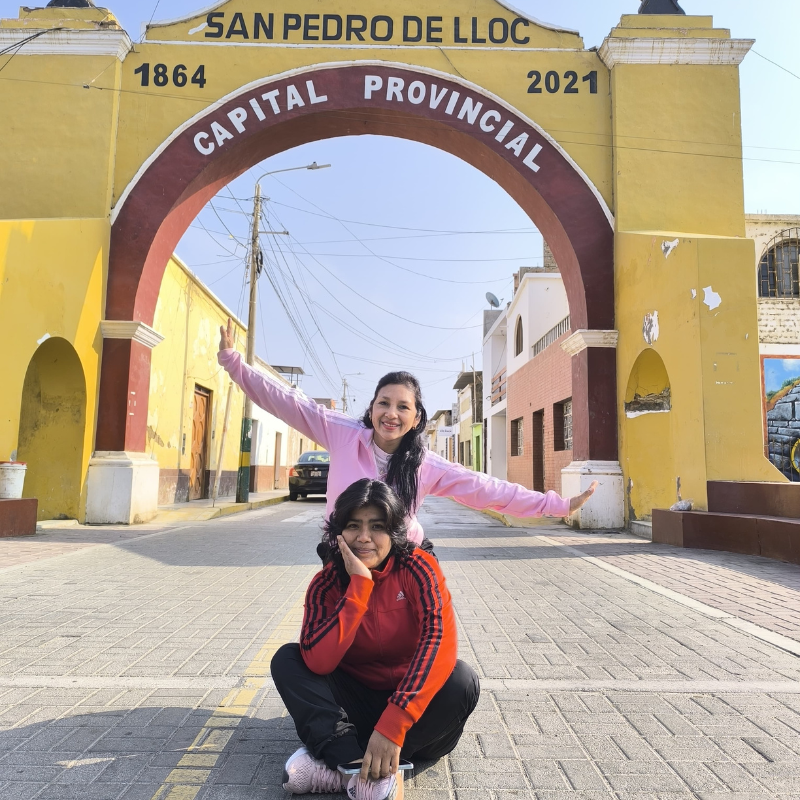 Dos turistas posando frente al gran arco amarillo de bienvenida de San Pedro de Lloc, capital provincial de Pacasmayo