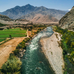 Fotografía aérea del río Majes fluyendo junto a campos de cultivo verdes entre los cerros áridos del Valle de Majes, Arequipa, Perú