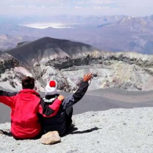 Dos excursionistas sentados al borde del cráter del Volcán Misti observando la caldera y el salar de Salinas al fondo en Arequipa, Perú
