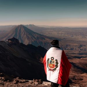 Montañista de espaldas cubierto con la bandera de Perú contempla el majestuoso volcán Misti desde la cumbre nevada del volcán Chachani en Arequipa