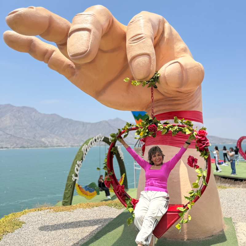 Turista sonriendo en un columpio de corazón suspendido de una escultura de mano gigante en el mirador de la Represa de Gallito Ciego