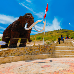 Escultura a escala real de un megaterio prehistórico junto a unas escalinatas de piedra y la bandera de Perú, en el complejo arqueológico de la cueva de Pikimachay, Ayacucho.