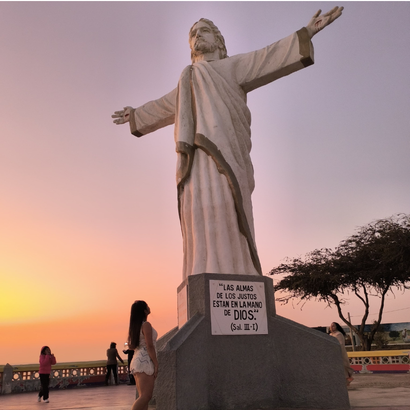 Turistas contemplando el monumento gigante del Cristo Redentor de Pacasmayo durante un atardecer con cielo rosado en La Libertad, Perú
