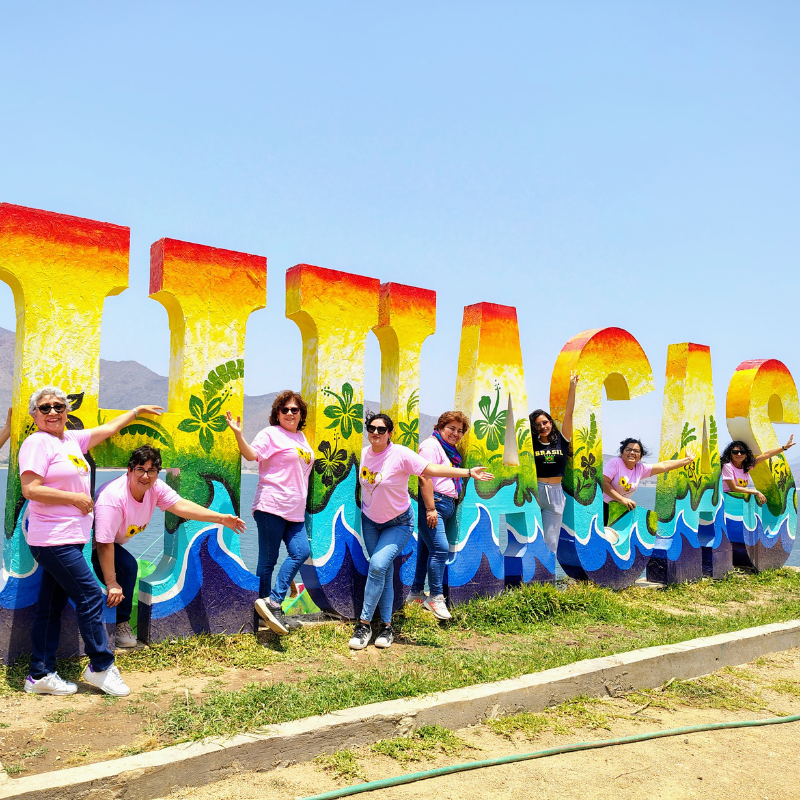 Grupo de turistas posando y saludando entre las coloridas letras gigantes de la palabra Cascas con vista al paisaje natural