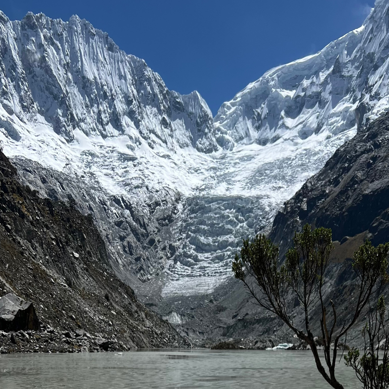 Impresionante vista panorámica de la Laguna Llaca reflejando un inmenso glaciar y las paredes de roca cubiertas de nieve del nevado Ranrapalca, en el Parque Nacional Huascarán, bajo un cielo azul despejado