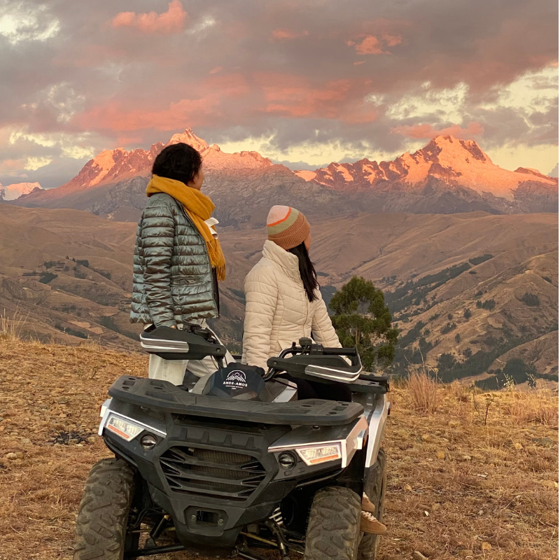 Dos mujeres sobre una cuatrimoto de contemplando el atardecer en las montañas de Huaraz